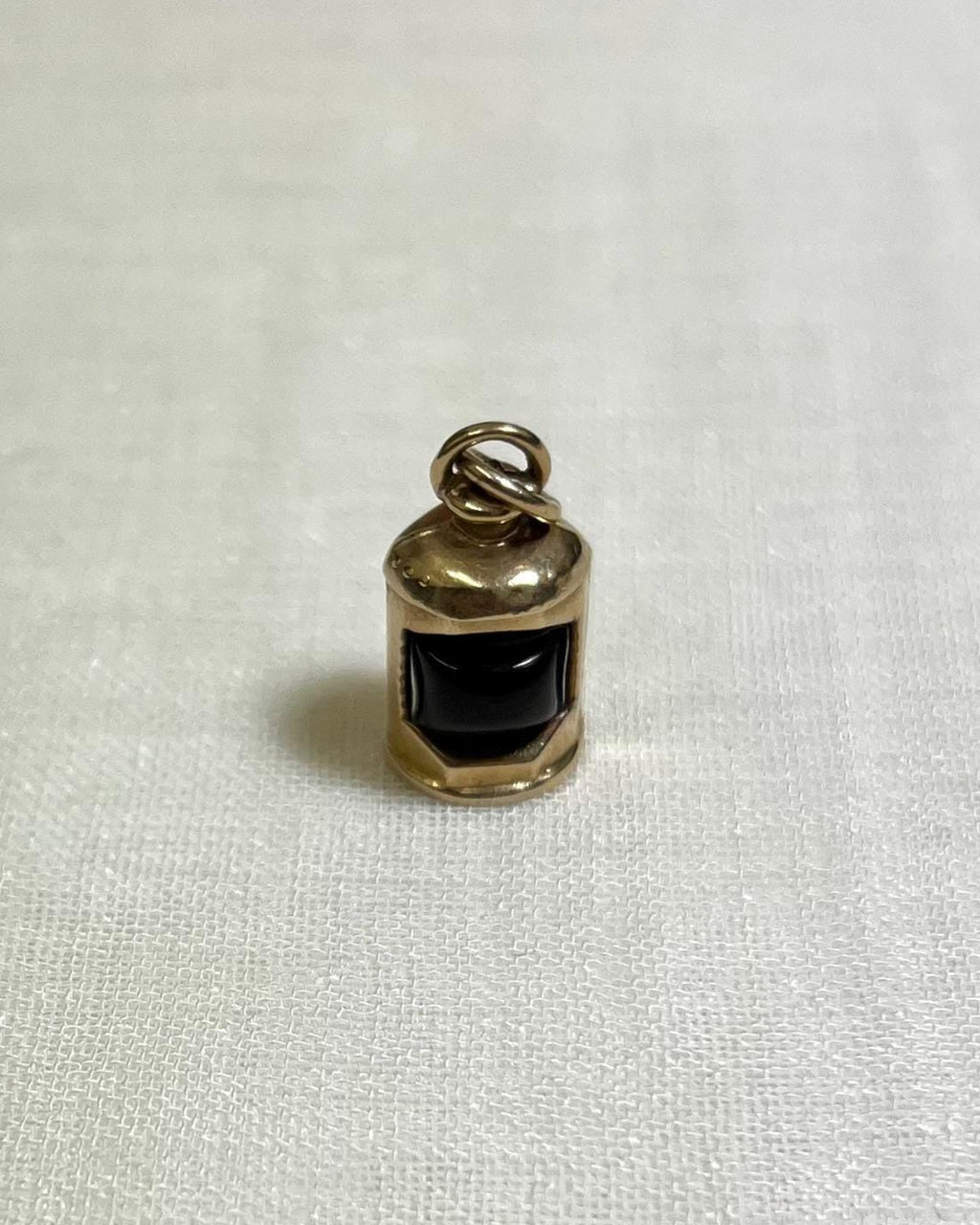 gold charm with dark red centre in the shape of ship lantern on white fabric background 