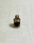 gold charm with dark red centre in the shape of ship lantern on white fabric background 