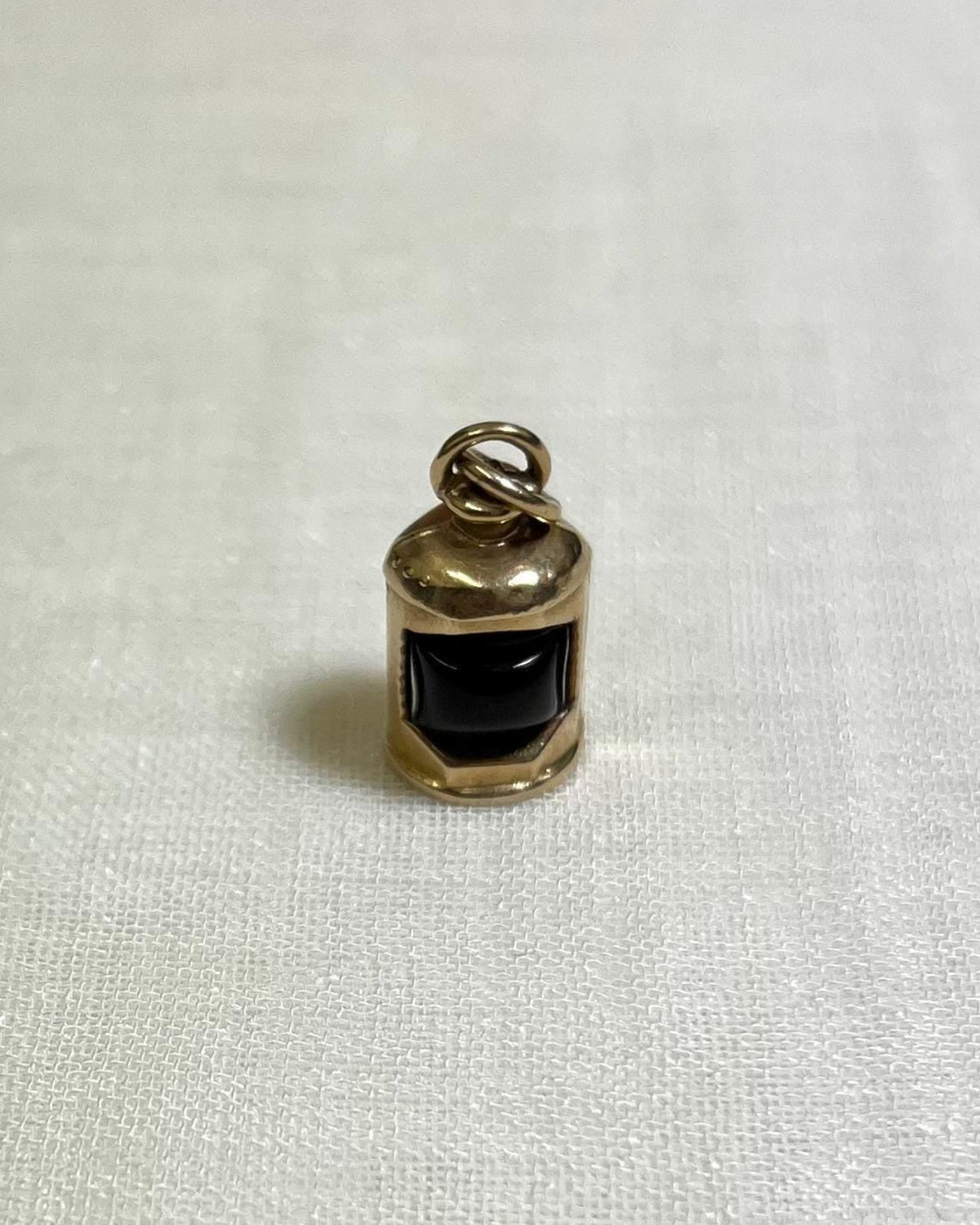 gold charm with dark red centre in the shape of ship lantern on white fabric background 