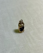 gold charm with dark red centre in the shape of ship lantern, on white fabric background 