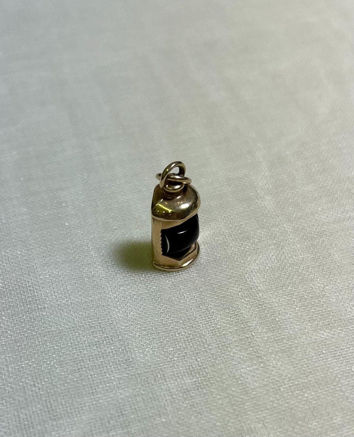 gold charm with dark red centre in the shape of ship lantern, on white fabric background 