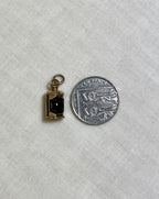 gold pendant with red centre next to ten pence coin for scale on white fabric background 