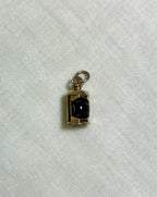 a gold charm with dark red centre on white fabric background 