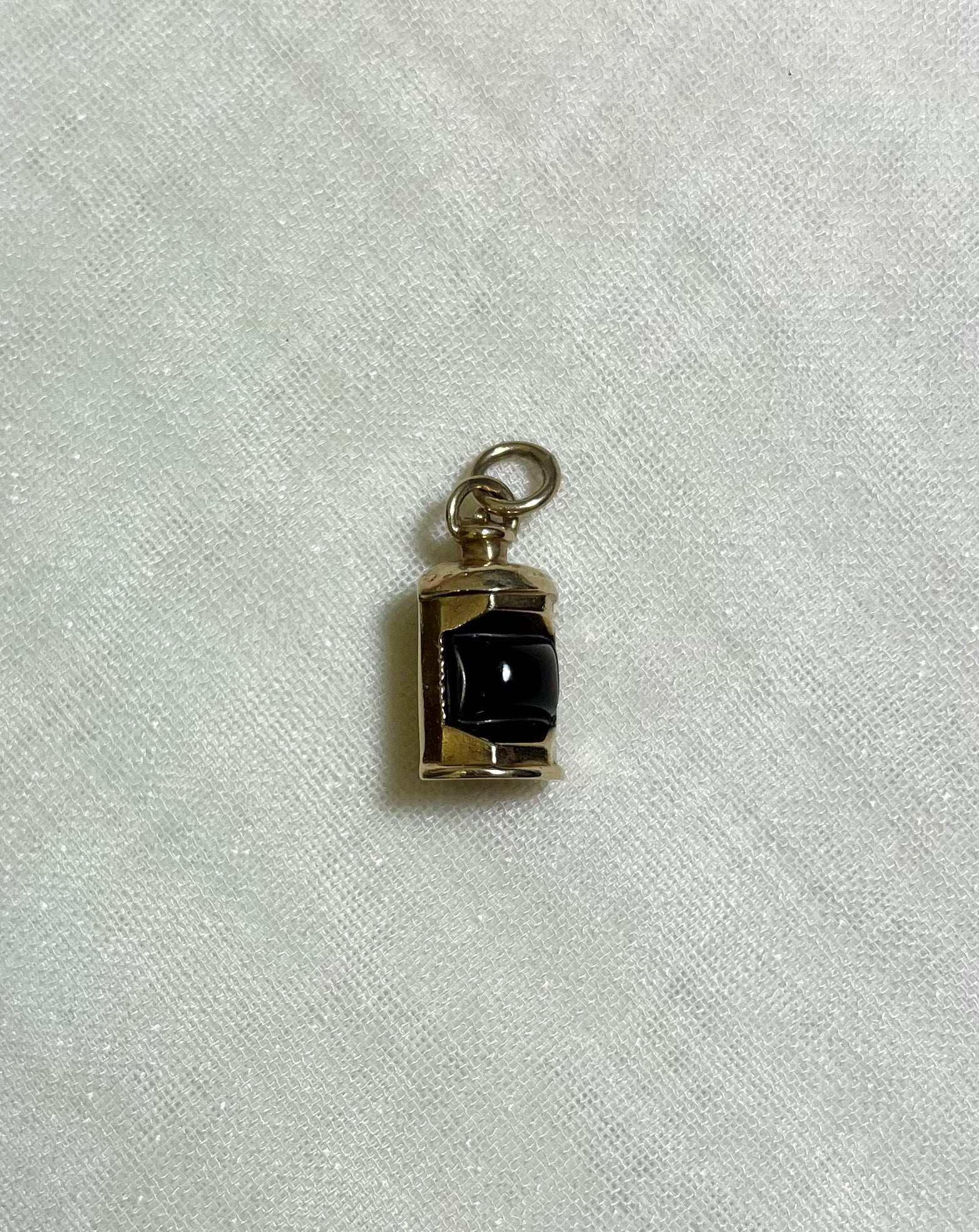 a gold charm with dark red centre on white fabric background 