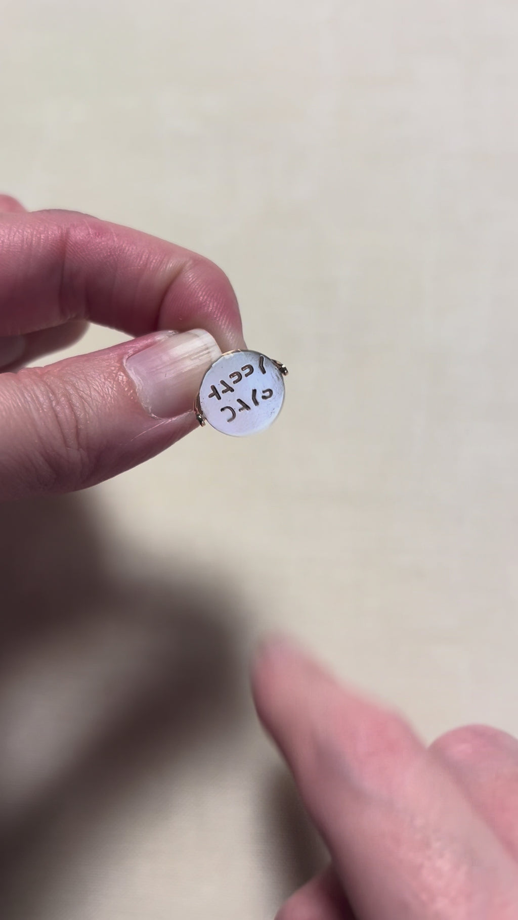 gold round pendant that is being spun to reveal message  ' happy dayss' above cream linen background