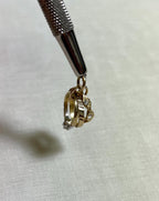Gold ring charm with a clear cubic zirconia stone, on white fabric background