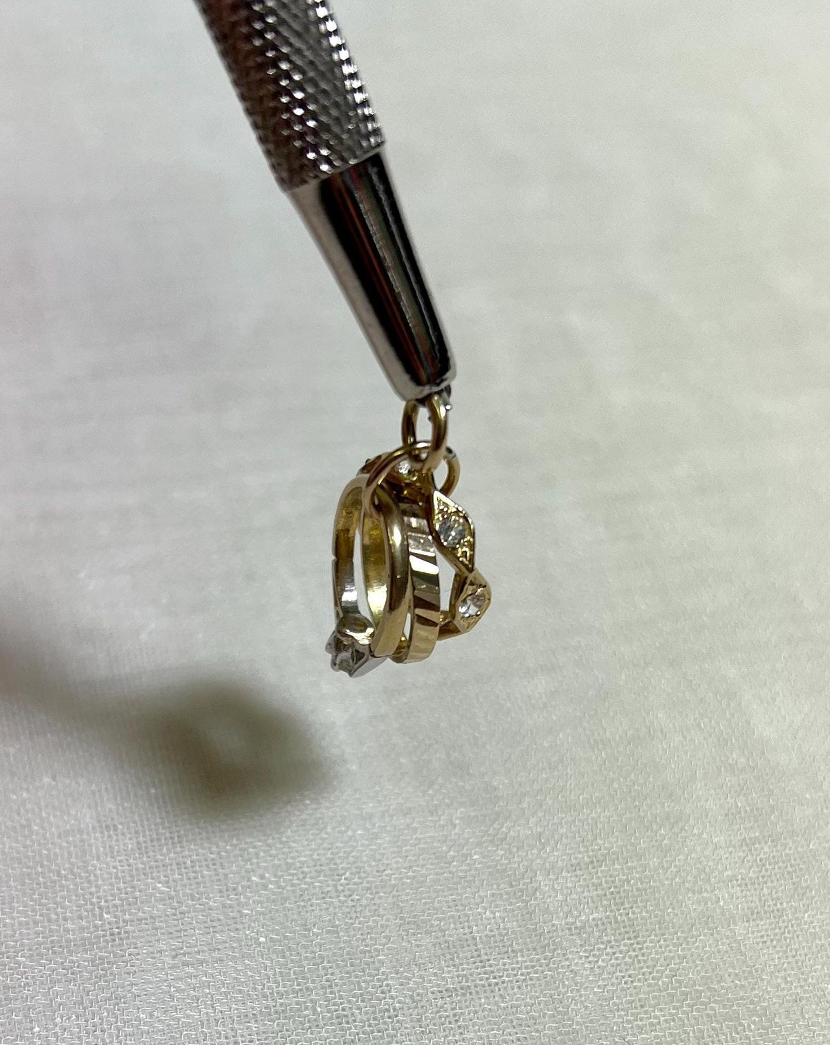 Gold ring charm with a clear cubic zirconia stone, on white fabric background