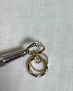a close up of clear cubic zirconia set gold ring charm held by metal tool above white fabric background