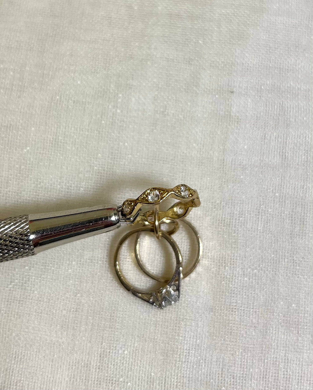 a close up of cubic zirconia set wave band charm held by metal tool above white fabric background 
