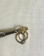a close up of cubic zirconia set wave band charm held by metal tool above white fabric background 