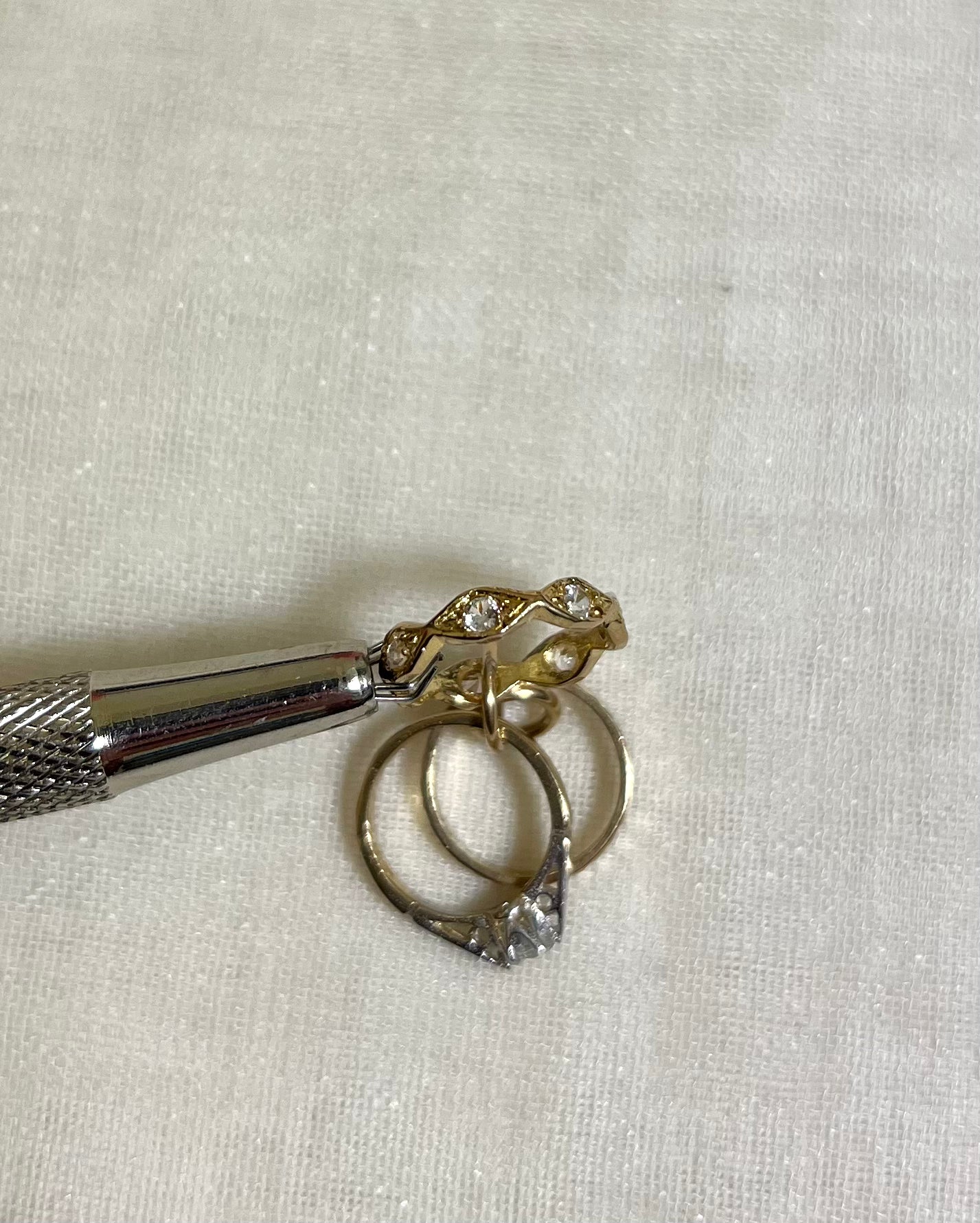 a close up of cubic zirconia set wave band charm held by metal tool above white fabric background 