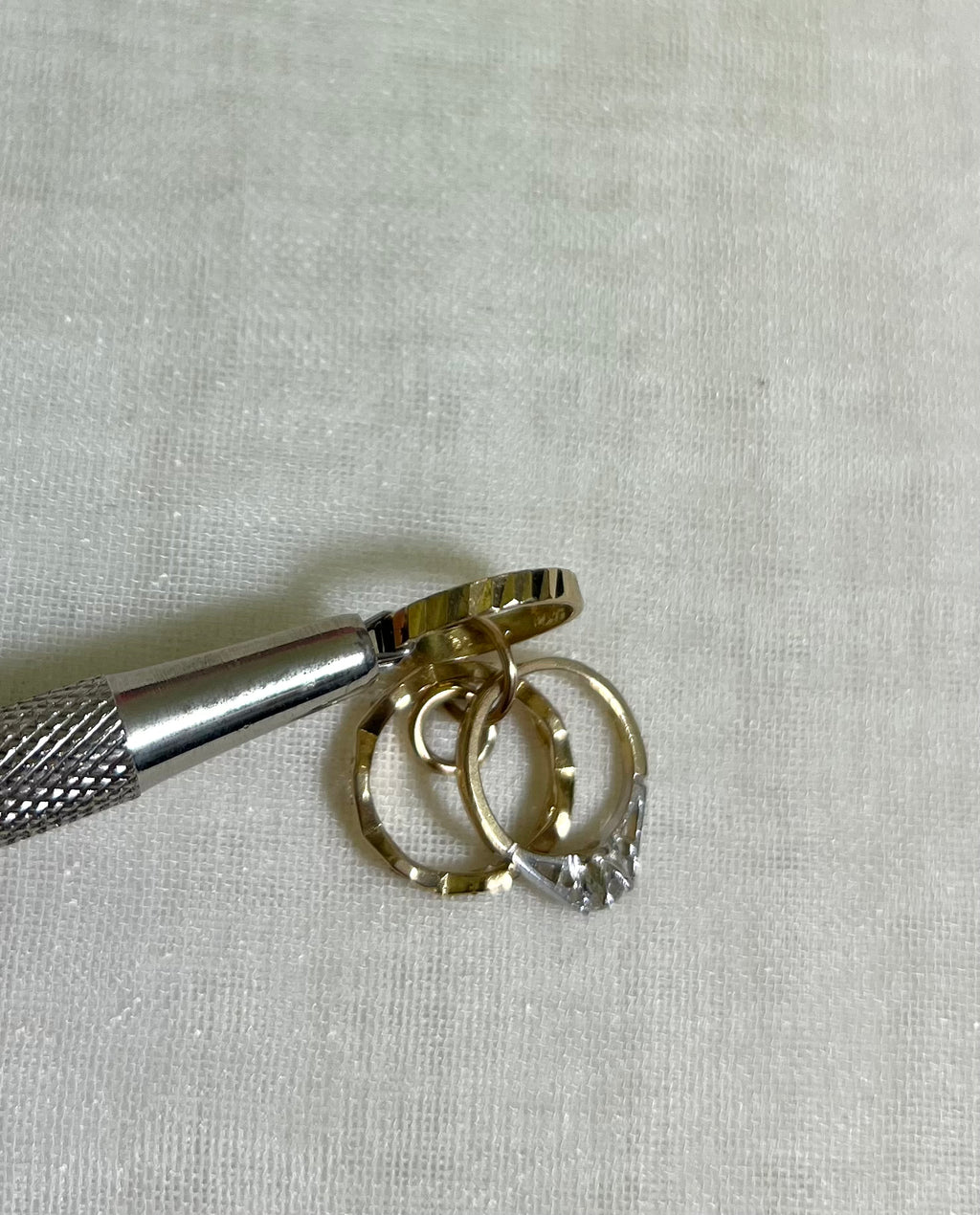 a close up of gold band charm held by metal tool on white fabric background 