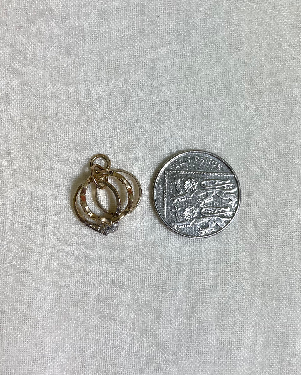 3 gold ring charm next to ten pence coin on white fabric background 