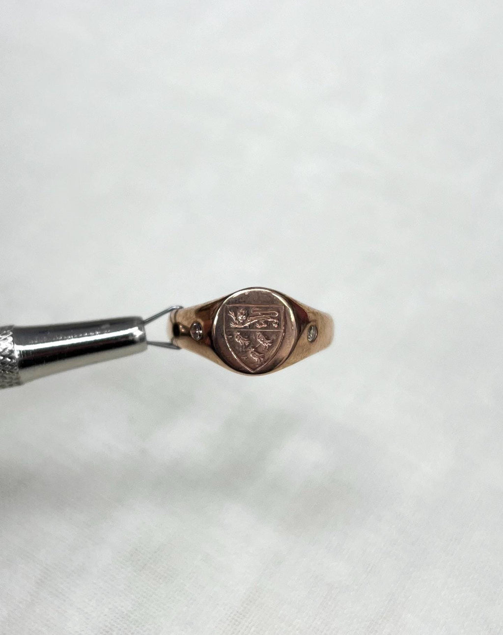 Rose gold ring with engraved design held by tweezers on a soft white background