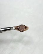 Rose gold ring with engraved design held by tweezers on a soft white background