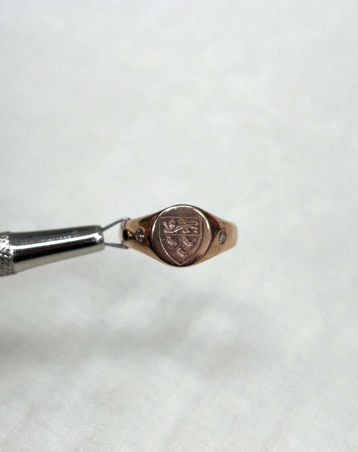 Rose gold ring with engraved design held by tweezers on a soft white background