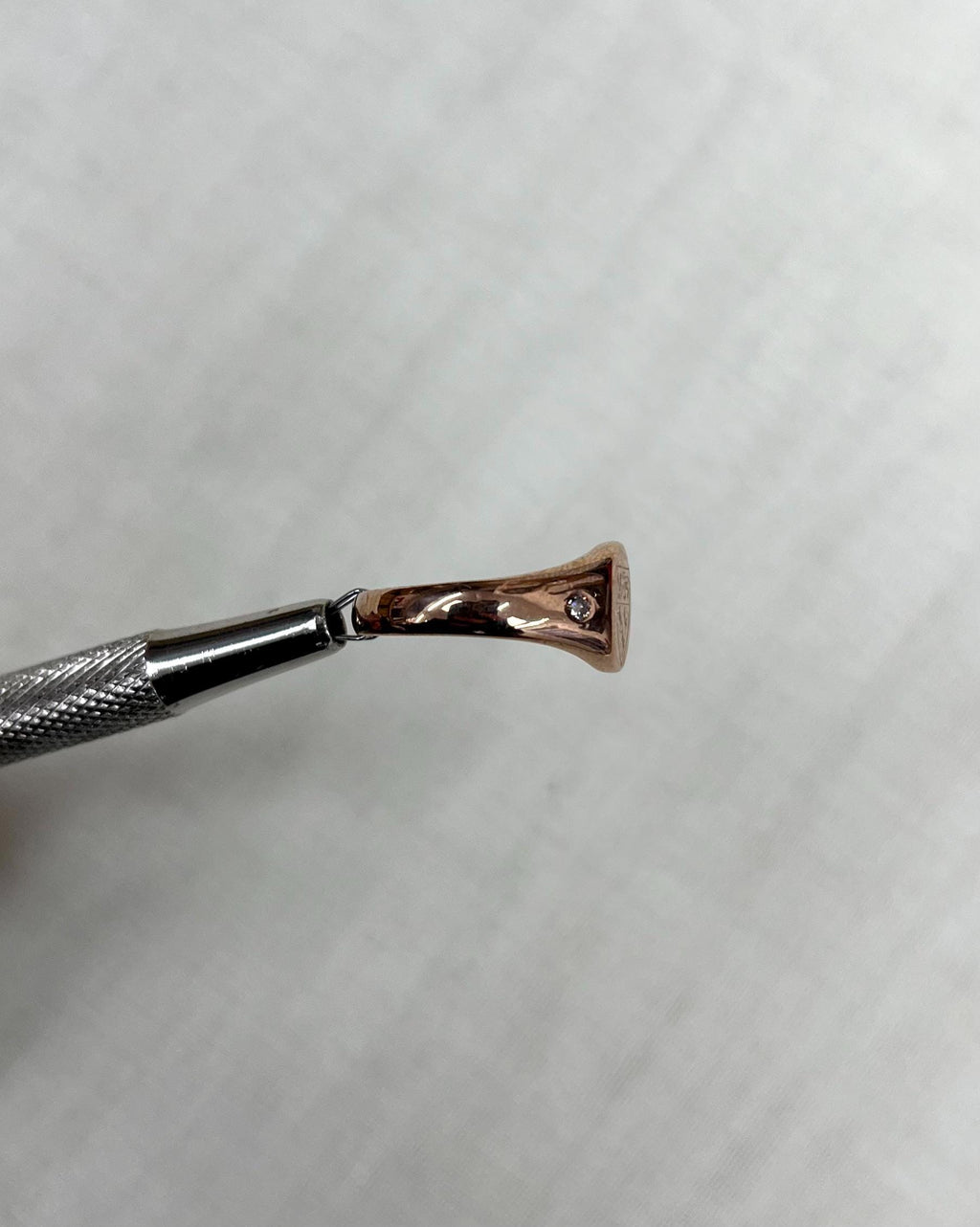 side view of rose gold ring held by metal tool above soft cream background
