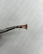 side view of rose gold ring held by metal tool above soft cream background