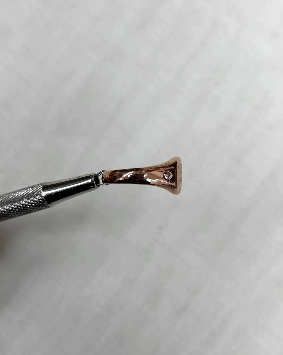 side view of rose gold ring held by metal tool above soft cream background
