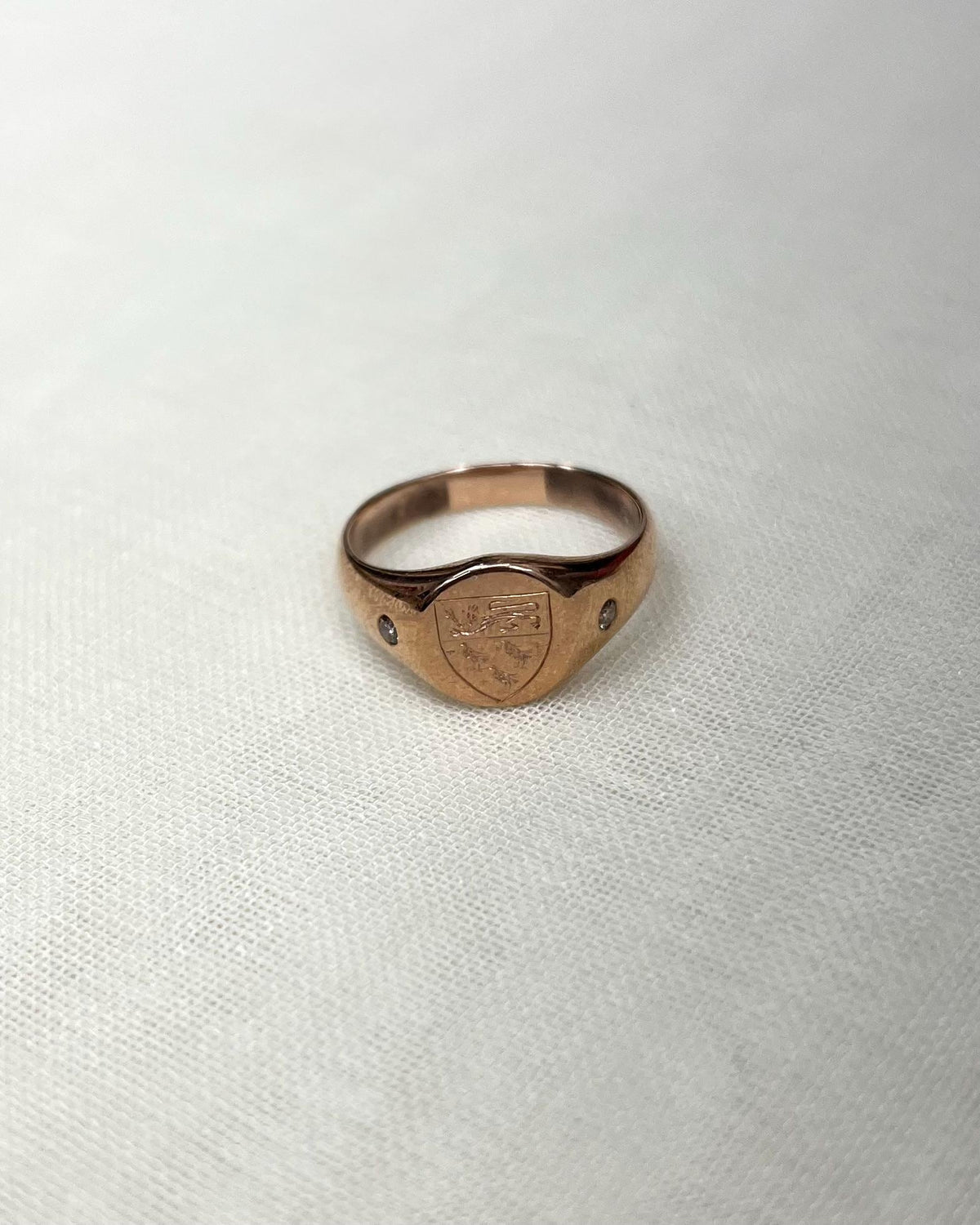 rose gold ring with shield crest engraving on white fabric background 