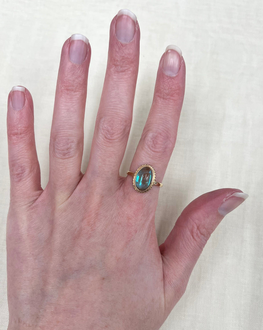 a gold ring with iridescent blue stone worn on hand, with soft white background 
