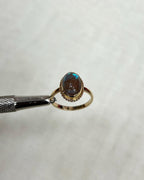 Gold ring with an oval gemstone held by tweezers on a light beige background