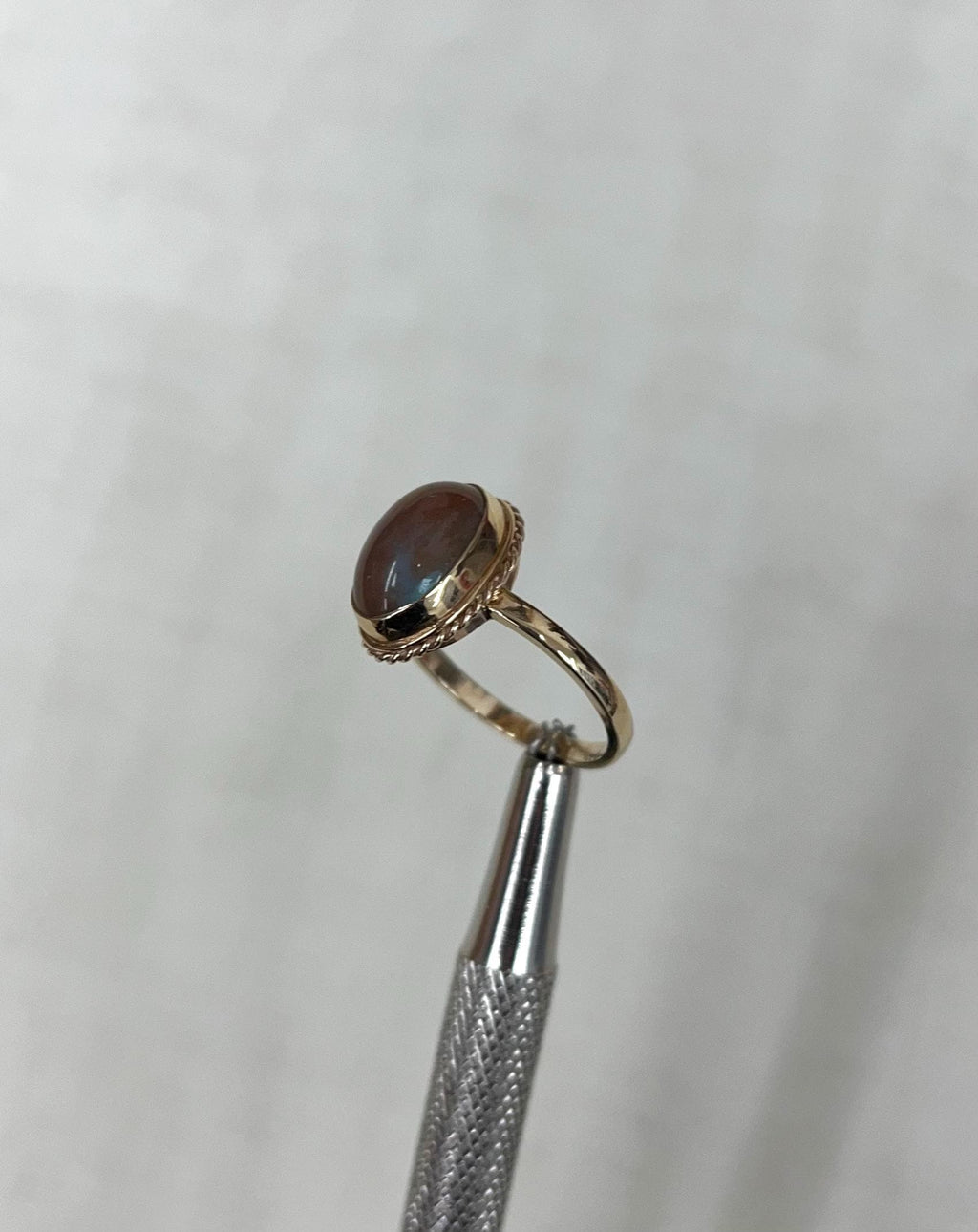 Gold ring with a brown gemstone and blue iridescence on a light beige background