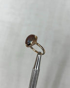 Gold ring with a brown gemstone and blue iridescence on a light beige background