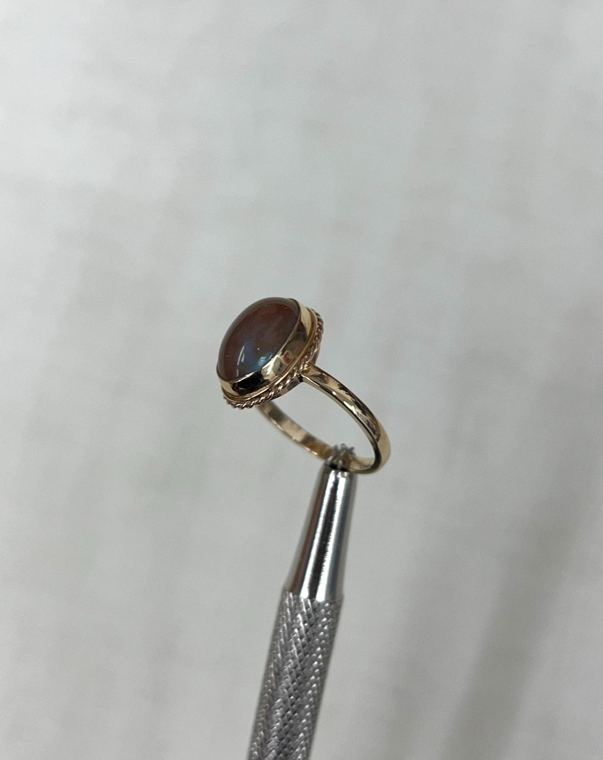 Gold ring with a brown gemstone and blue iridescence on a light beige background