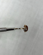 side view of gold ring with brown stone, held by metal tool above light beige background 