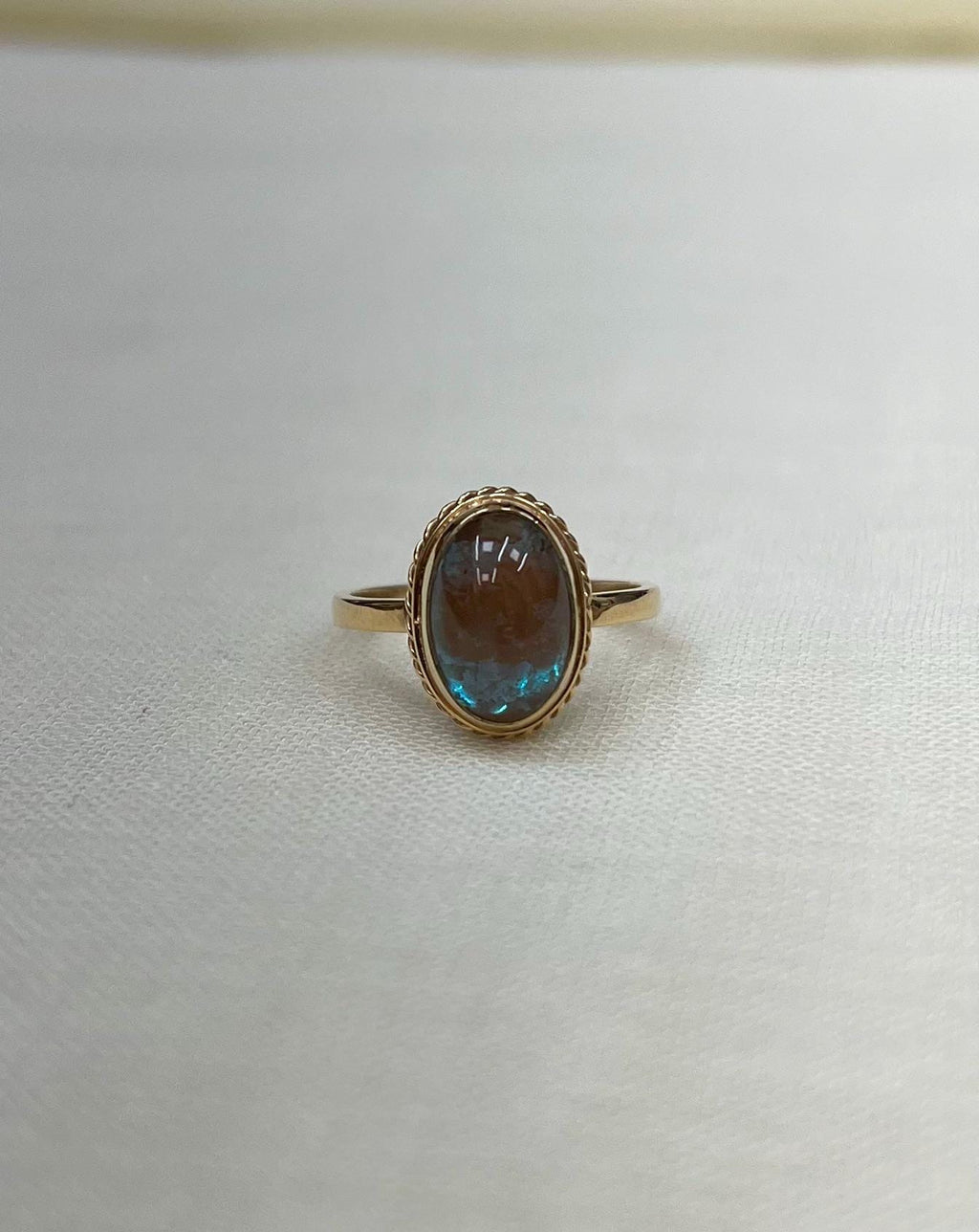 Gold ring with a blue iridescent gemstone on a white fabric background