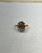 Gold ring with a blue iridescent gemstone on a white fabric background