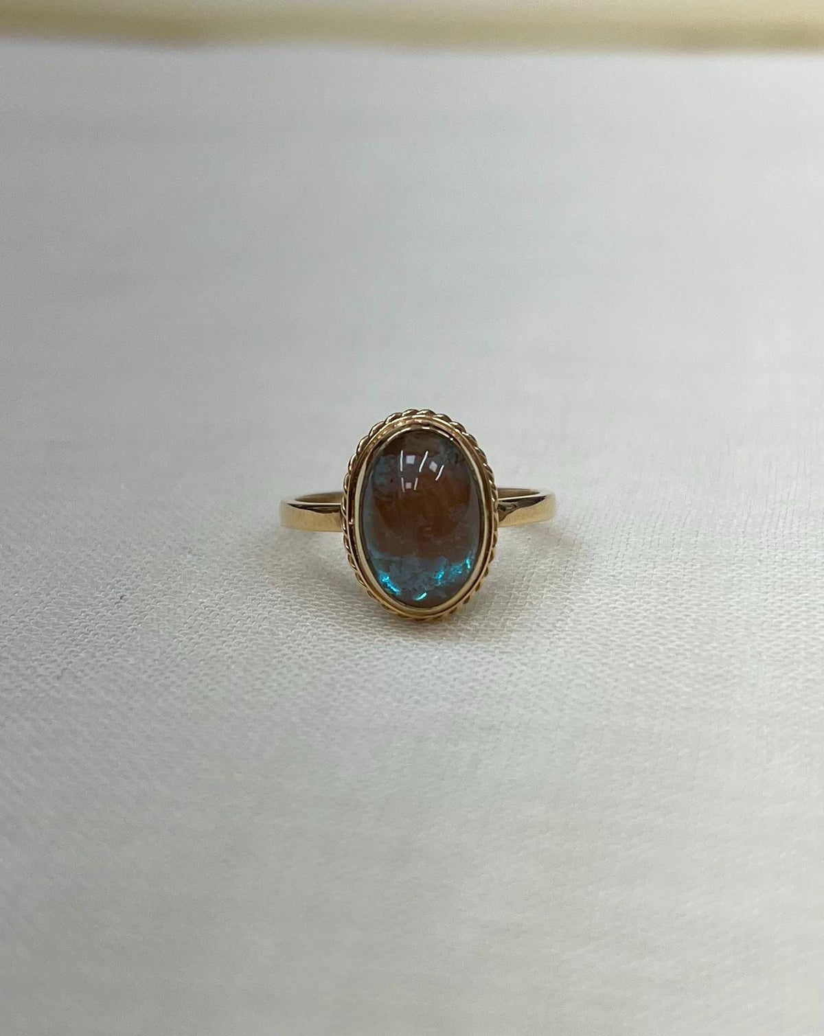 Gold ring with a blue iridescent gemstone on a white fabric background