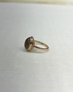 A gold ring with an oval brown and blue iridescent cabochon gemstone, resting on a textured white fabric surface.