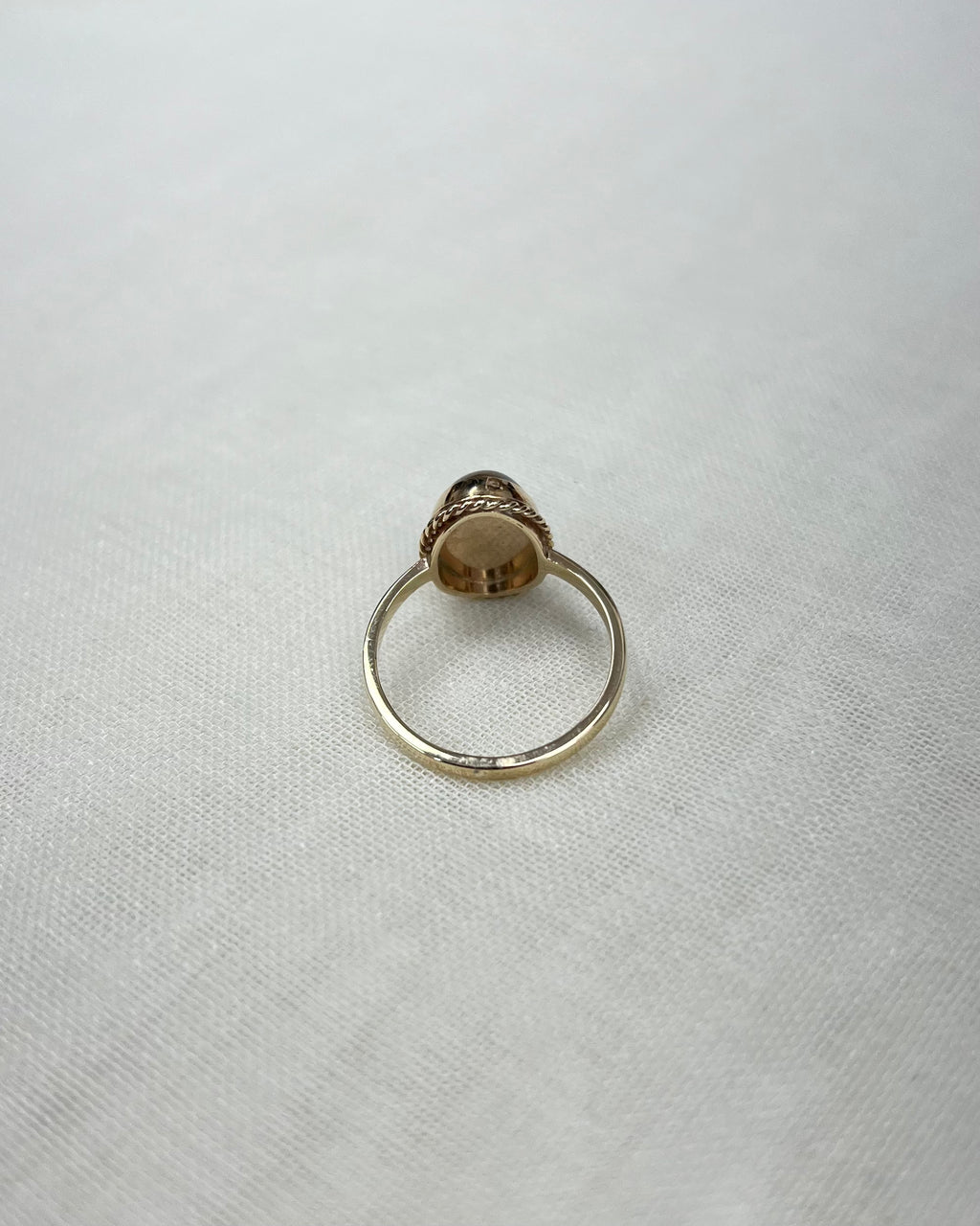 back view of gold ring, on white fabric surface 