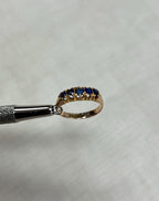 Gold ring with blue stones being held by silver tool on beige background