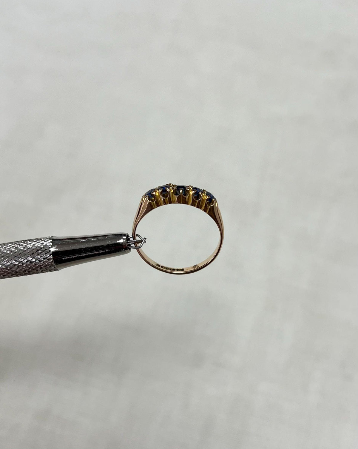 Gold ring being held with a tool on a light beige background