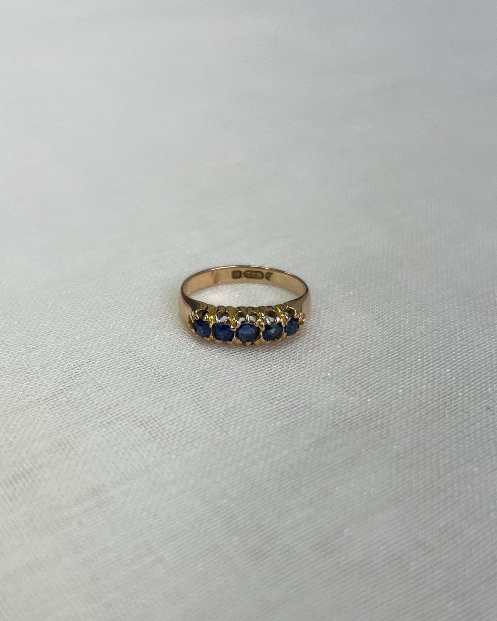 Gold ring with blue stones on a light beige background