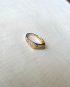 A gold signet ring with engraved geometric patterns and a small star detail set with diamond, resting on a textured white fabric background.