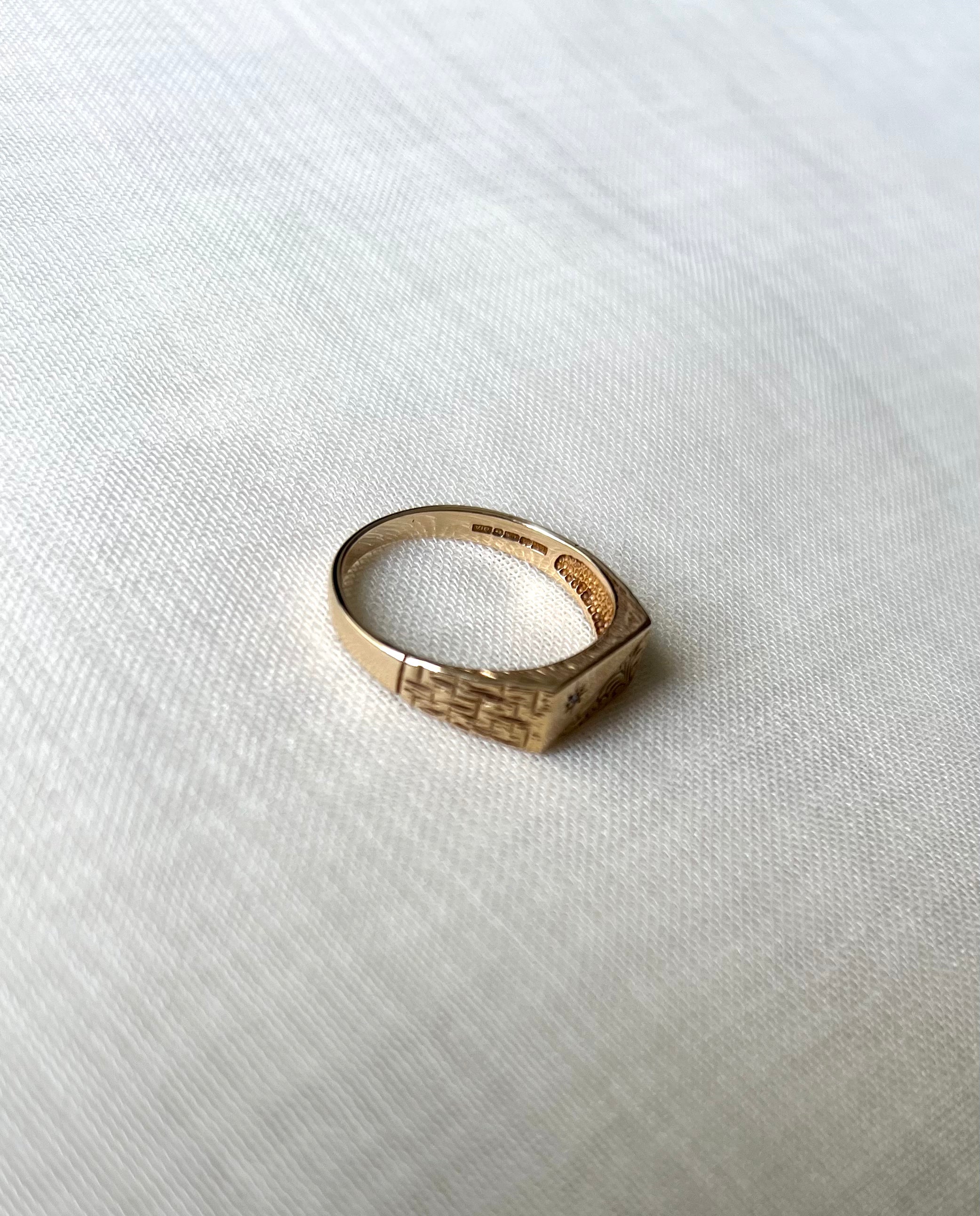 A textured gold signet ring with visible hallmark resting on a white linen fabric background.