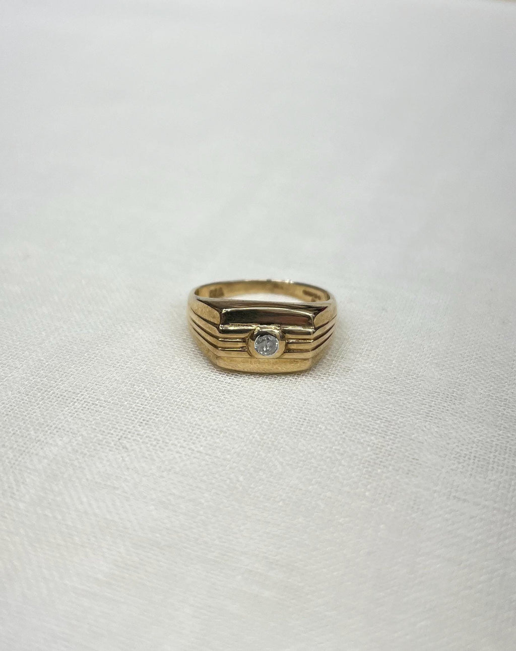 gold signet ring with diamond centre on white fabric background 