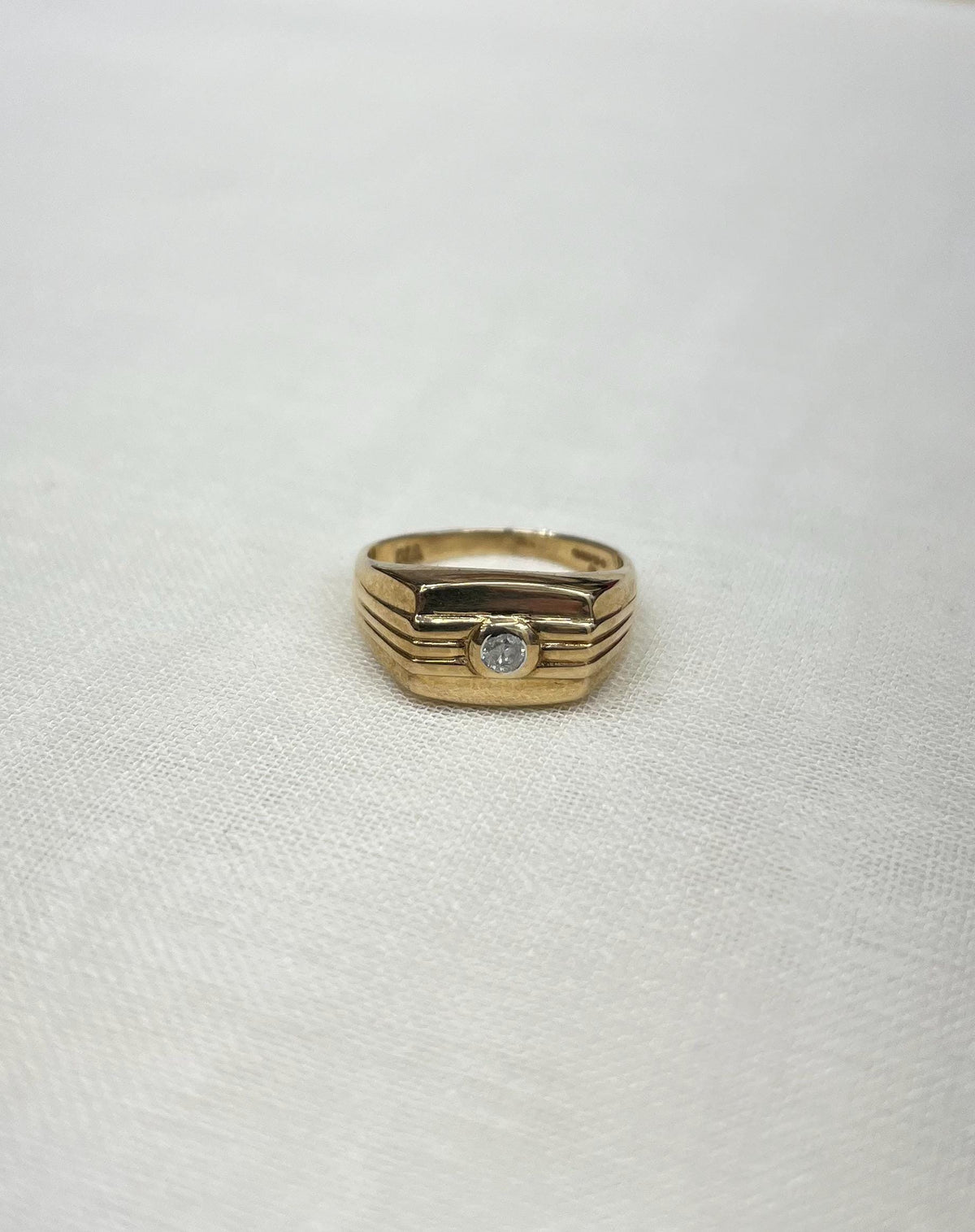 gold signet ring with diamond centre on white fabric background 