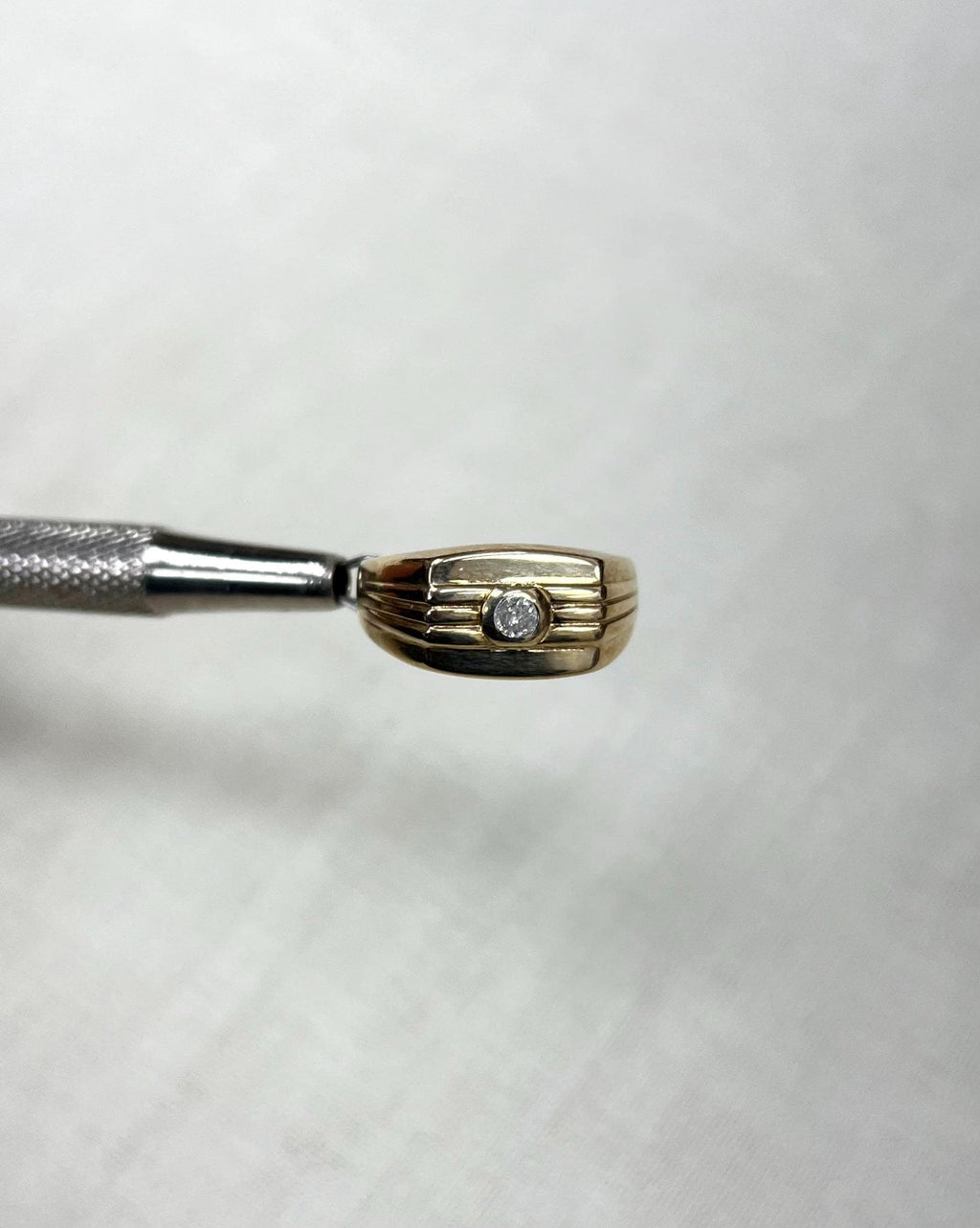 gold ring set with diamond, held by silver tool above white background 