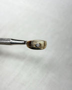 gold ring set with diamond, held by silver tool above white background 