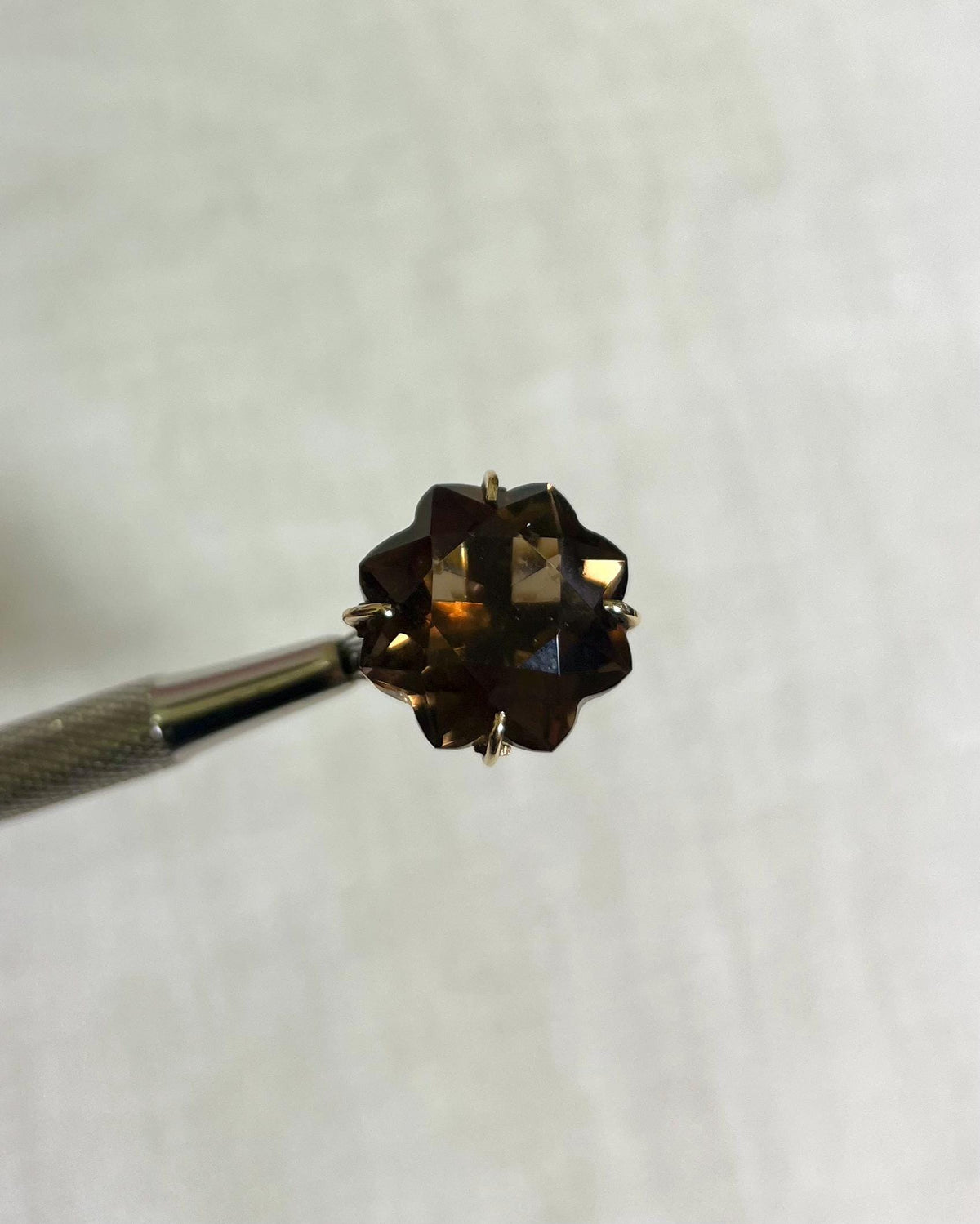 gold ring with large brown gemstone held by silver tool above white background 