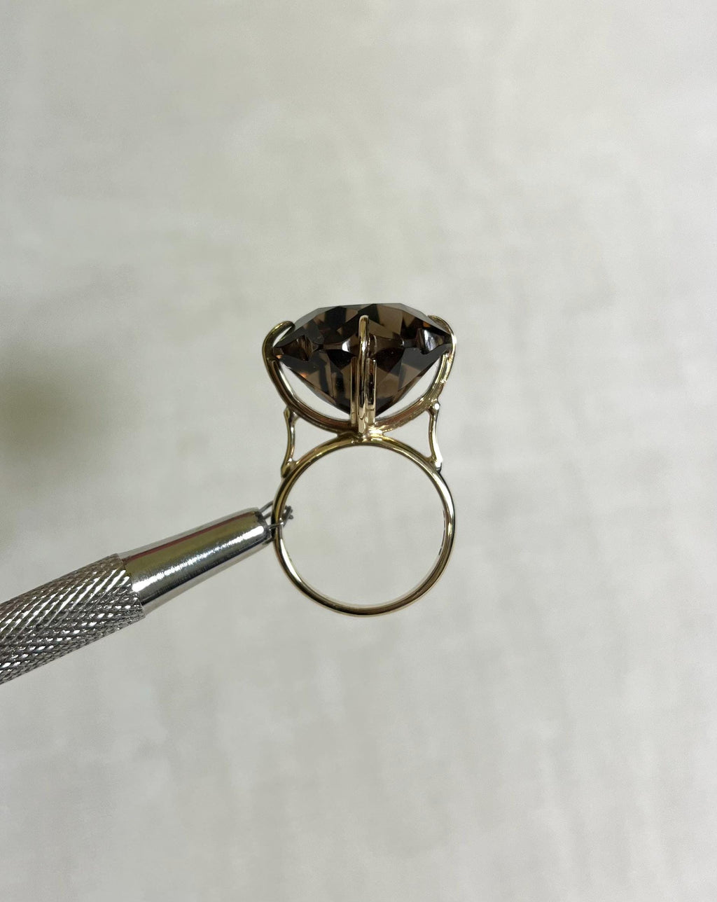 large statement ring with brown smokey quartz gemstone, held by silver tool above white background
