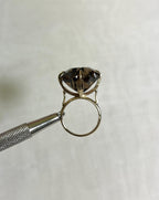 large statement ring with brown smokey quartz gemstone, held by silver tool above white background