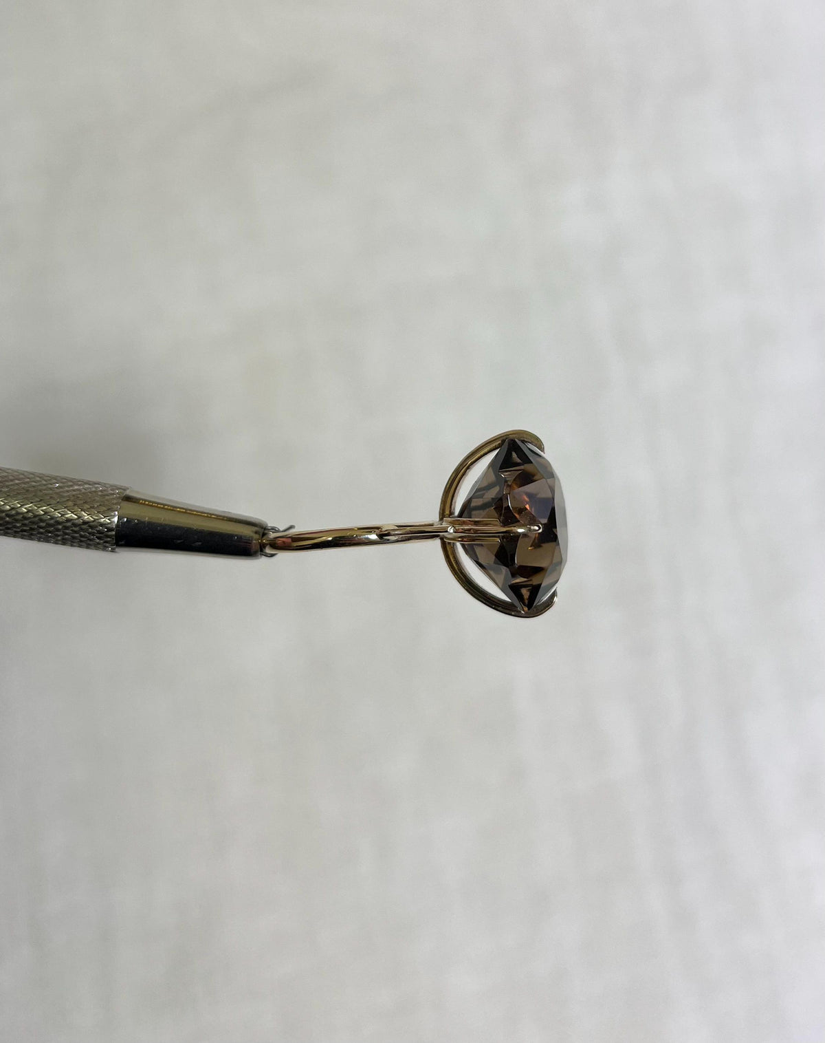 side view of gold ring with large smokey quartz, held by silver tool above white background