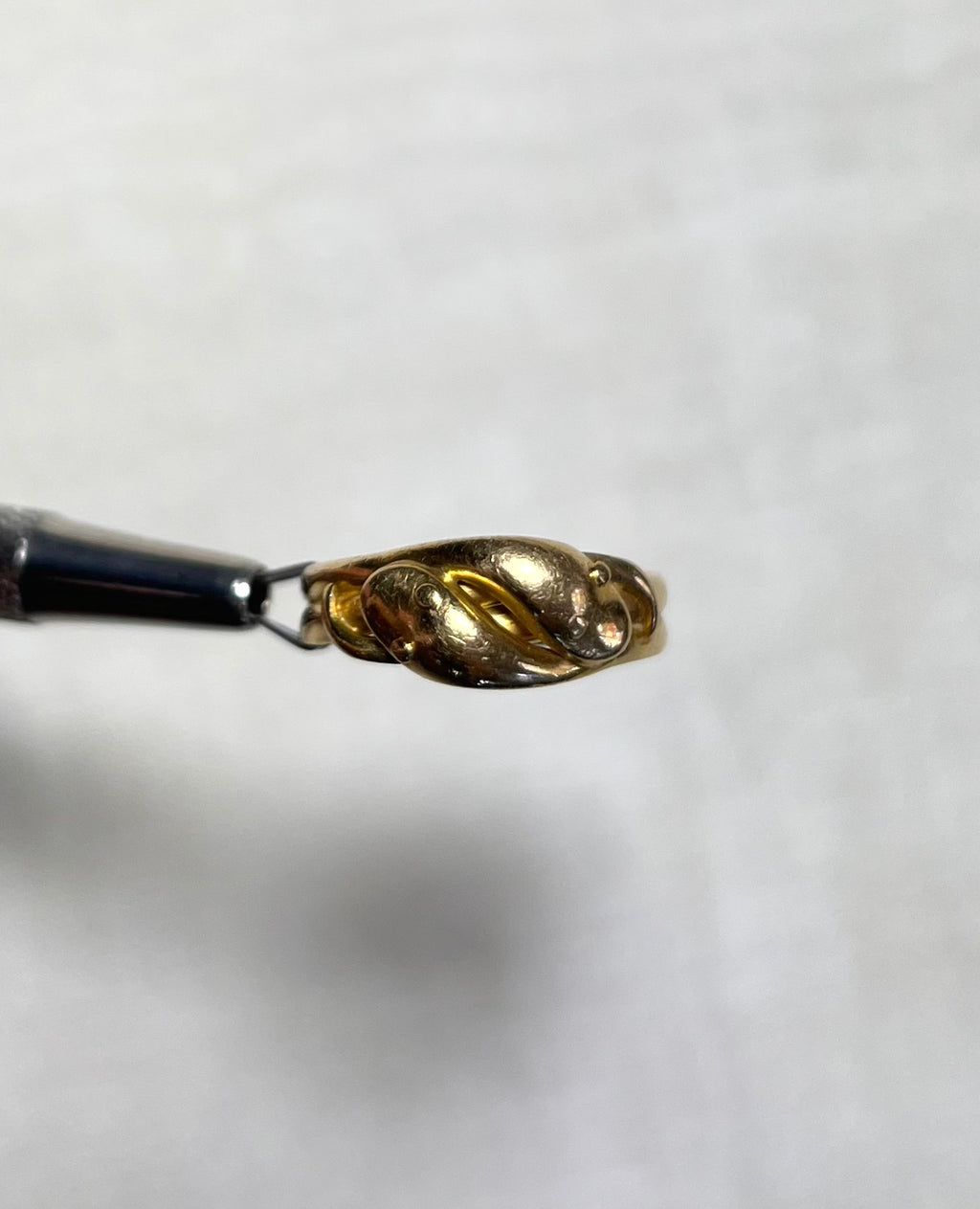 gold ring with two snake heads, held by silver jewellers tool above soft cream background