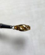 gold ring with two snake heads, held by silver jewellers tool above soft cream background